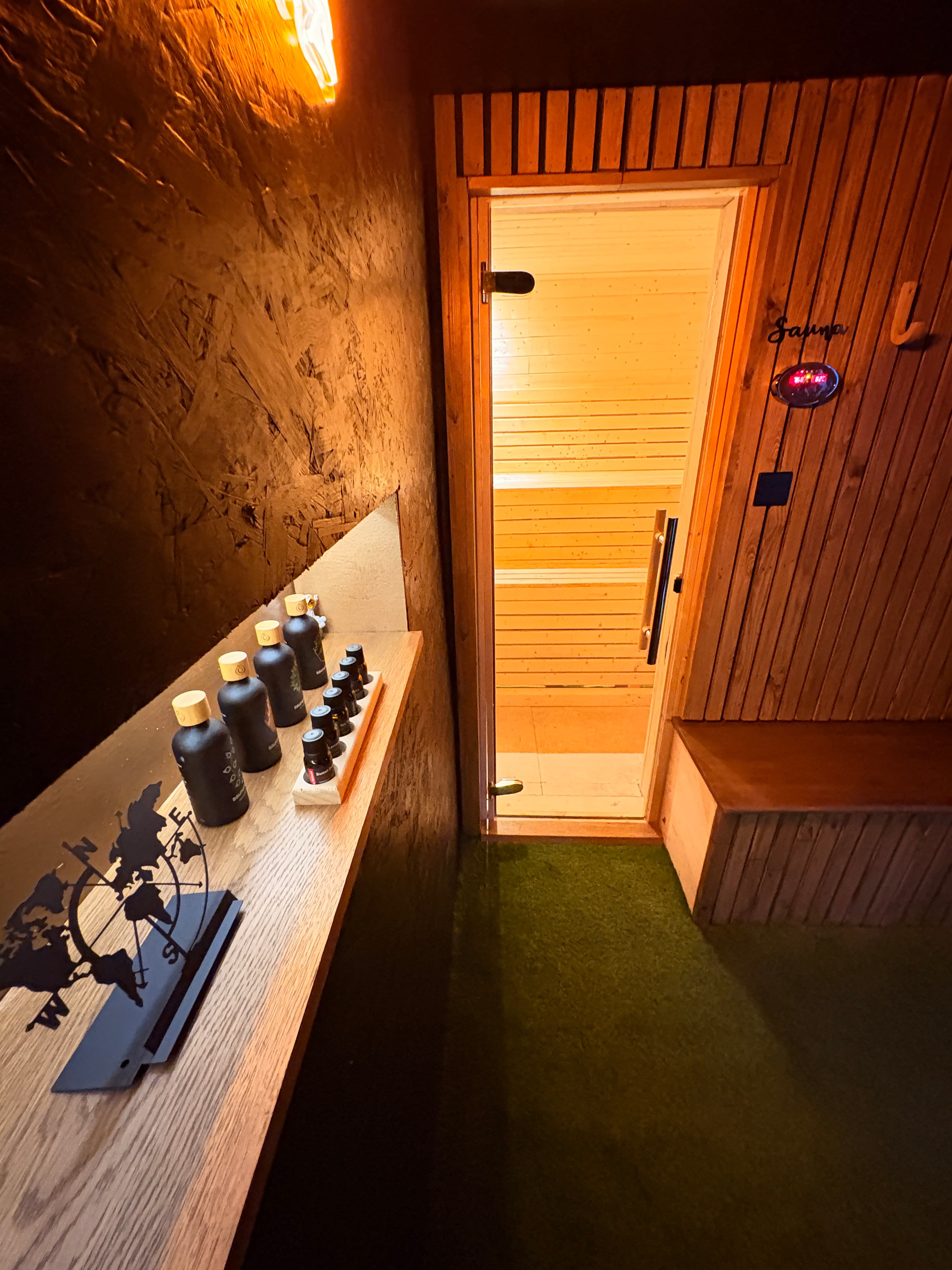 Wooden sauna interior with a glass window and essential oil bottles on a shelf.